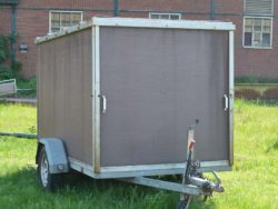 Rustic utility trailer on green grass, perfect for outdoor projects near an industrial backdrop.