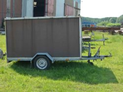 Vintage utility trailer on green grass near rustic industrial buildings, showcasing a blend of nature and history.