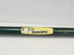 Green telescopic pole with yellow label, ideal for reaching high places and versatile tasks.