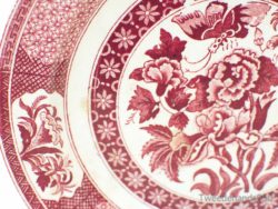 Vintage red ceramic plate with floral and butterfly designs, showcasing exquisite craftsmanship and charm.