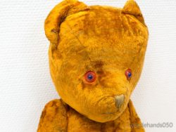 Vintage teddy bear with warm orange fur and soulful blue eyes, evoking childhood memories.