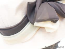 Chic cream hat with luxurious dark bow, perfect for elegant events and stylish occasions.