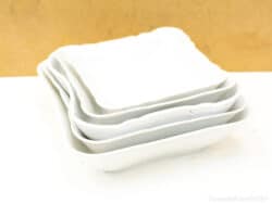 Elegant stack of four smooth white square plates for stylish dining experiences.