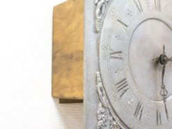 Vintage metallic wall clock with Roman numerals and wooden base, perfect for elegant décor.