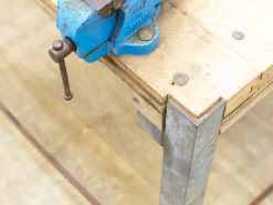 Sturdy blue vise on a rustic wooden workbench, perfect for skilled craftsmanship and projects.