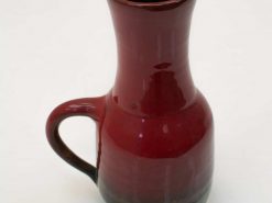 Elegant deep red ceramic pitcher with a glossy finish and graceful handle, perfect for decoration.