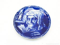 Elderly woman reading on a decorative blue porcelain plate, representing wisdom and beauty in art.