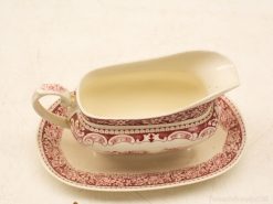 Classic red and white gravy boat with matching saucer for elegant dining occasions.