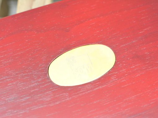 Vintage wooden table featuring a polished brass plate and rich red finish, showcasing elegant craftsmanship.