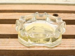 Vintage glass ashtray with yellow liquid on rustic wooden table, evoking nostalgia and charm.