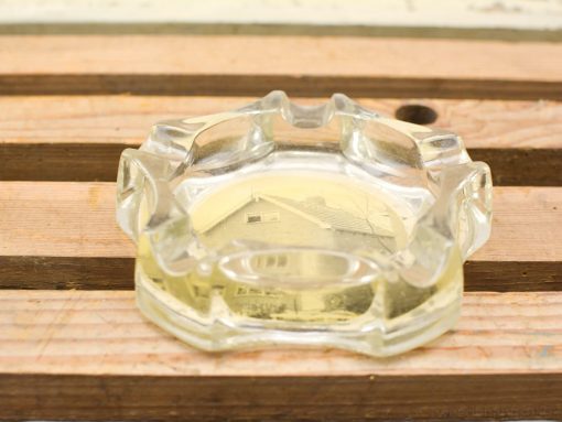 Vintage glass ashtray with yellow liquid on rustic wooden table, evoking nostalgia and charm.