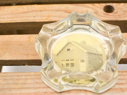 Vintage glass ashtray with nostalgic house photo on rustic wooden surface for charming decor.