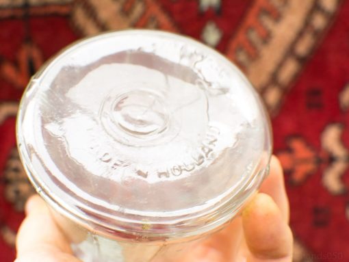 Charming vintage glass jar with Made in Holland lid against rich patterned fabric backdrop.