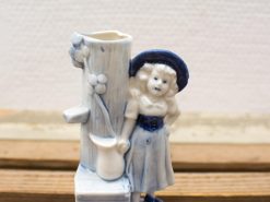 Charming ceramic girl figurine by tree stump, evoking nostalgia and folk art beauty.