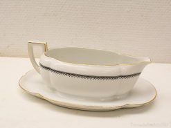 Elegant white porcelain gravy boat with black accents and gold rim, on matching saucer.