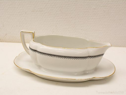 Elegant white porcelain gravy boat with black accents and gold rim, on matching saucer.