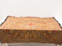 Elegant vintage paisley tablecloth with fringe in warm tones, perfect for any decor.