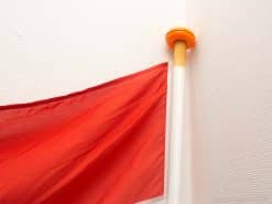 Vibrant red flag in corner of modern room with white pole and orange fixture.