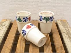 Vintage floral ceramic cups set, vibrant designs on rustic wooden surface, perfect for festive settings.