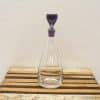 Elegant glass decanter with purple stopper, perfect for serving and showcasing beverages.