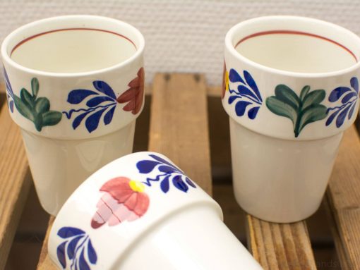 Colorful handmade ceramic cups on rustic wood, showcasing artistic floral designs and charming craftsmanship.