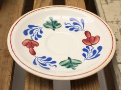 Vibrant ceramic plate with floral design in red, green, and blue on a rustic wooden surface.