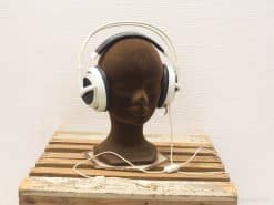 Modern white headphones on a dark mannequin head atop rustic wooden platform.