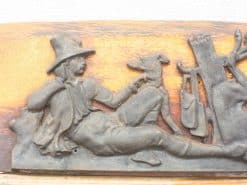 19th-century man relaxing with dog in detailed wooden relief sculpture. Perfect for rustic decor.