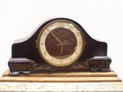 Elegant vintage wooden mantel clock with curved design and polished metallic accents.