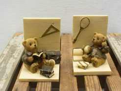 Adorable teddy bears, one reading and one playing sports, on a rustic wooden base.