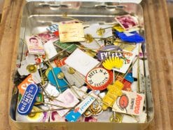 Colorful vintage enamel pins, badges, and photo cards in a nostalgic metal tin collection.