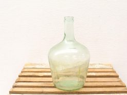 Vintage green glass bottle with teardrop shape, showcasing artisanal imperfections on wooden surface.