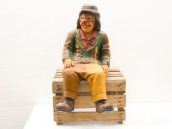 Whimsical wooden clown on crate: a charming vintage circus decoration for any space.