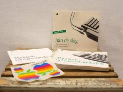 Vintage Macintosh manuals and colorful Apple stickers on a rustic wooden surface.