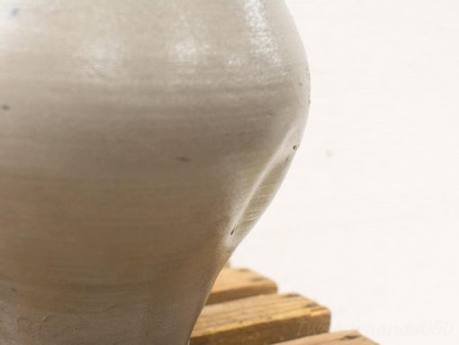 Elegant gray ceramic vase with unique imperfections on a warm wooden surface.