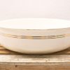 Elegant white bowl with gold and charcoal stripes on a rustic wooden base.