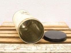 Vintage metal canister with black lid on weathered wooden surface, exuding rustic charm.