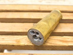 Antique brass cylinder with three holes, beautifully polished, resting on a rustic wooden surface.