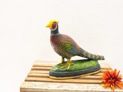 Vibrant pheasant figurine on grass base, accented with bright orange flower for decorative appeal.