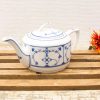 Elegant porcelain teapot with blue floral design, accompanied by a vibrant flower on wood.