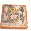 Intricate terracotta ceramic tile featuring heraldic coat of arms and vibrant floral motifs.