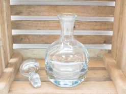 Elegant glass decanter with stopper on rustic wood, perfect for serving wine or spirits.