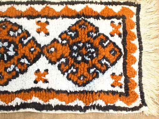 Vibrant geometric vintage textile in orange and black with elegant fringe, perfect for any decor.