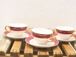 Elegant vintage tea cups and saucers with burgundy and gold accents on a rustic surface.