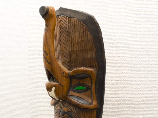 Intricate wooden mask with vibrant green eyes, showcasing rich cultural heritage and artistry.