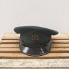 Elegant green military cap with crown emblem on rustic wooden base, showcasing craftsmanship and tradition.