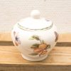 Elegant porcelain container adorned with vibrant painted fruits and butterflies on a white background.