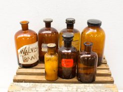 Vintage brown glass bottles on a wooden crate, featuring a notable WALVIS TRAAN label.