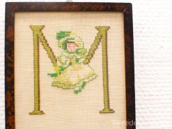 Whimsical vintage embroidery of letter M with a girl swinging in a yellow dress.