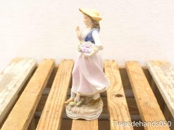 Charming porcelain figurine of a young woman in pastoral attire with flowers.